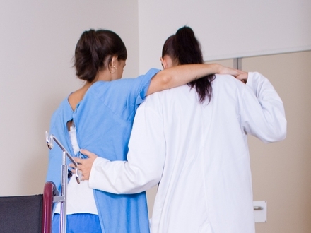 Doctor assists a patient in a blue hospital gown walking