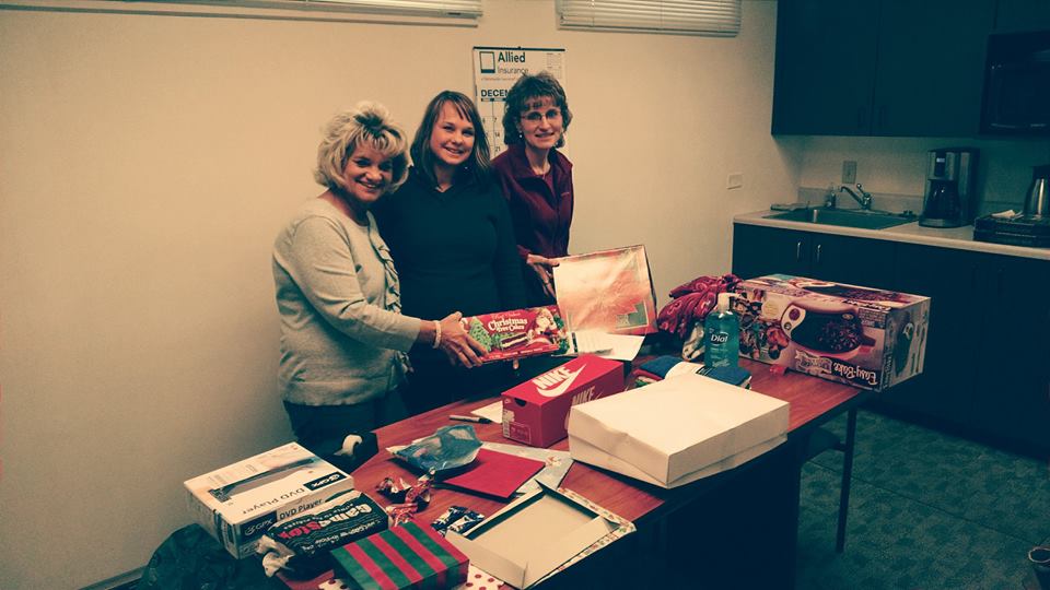 Three staff members by the table of wrapped christmas gifts for the St. Vincent De Paul's Adopt-a-Family program.